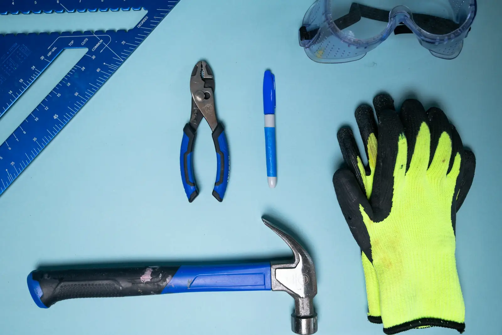 Hammer, pliers, marker, gloves, and safety glasses laid out for a repair job